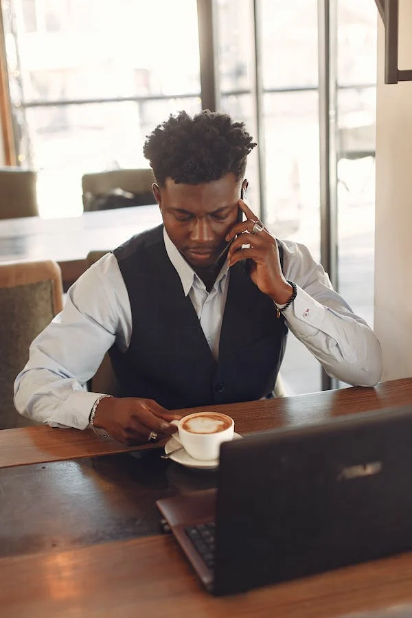 male drinking coffee on the phone and using a lap top